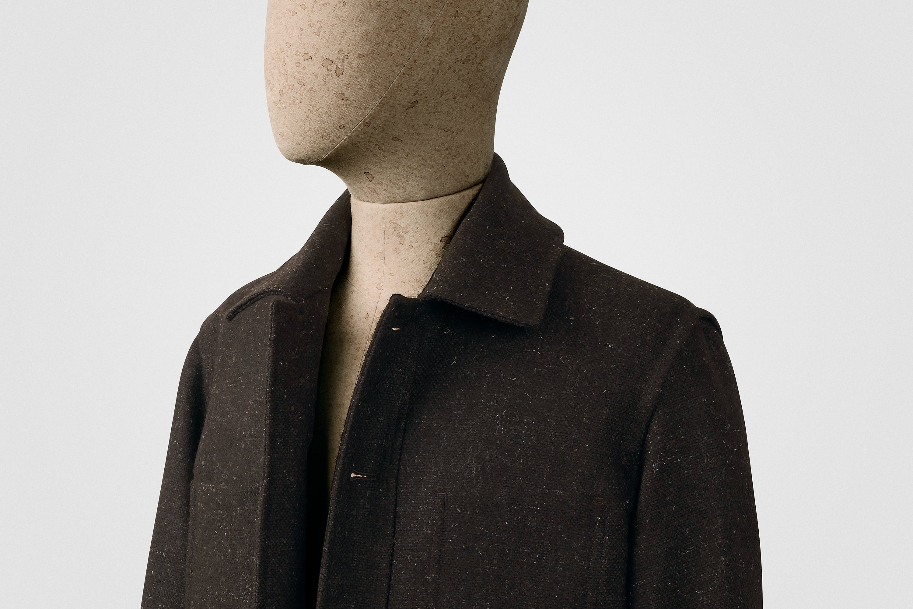 Mannequin wearing a dark brown coat against a plain background